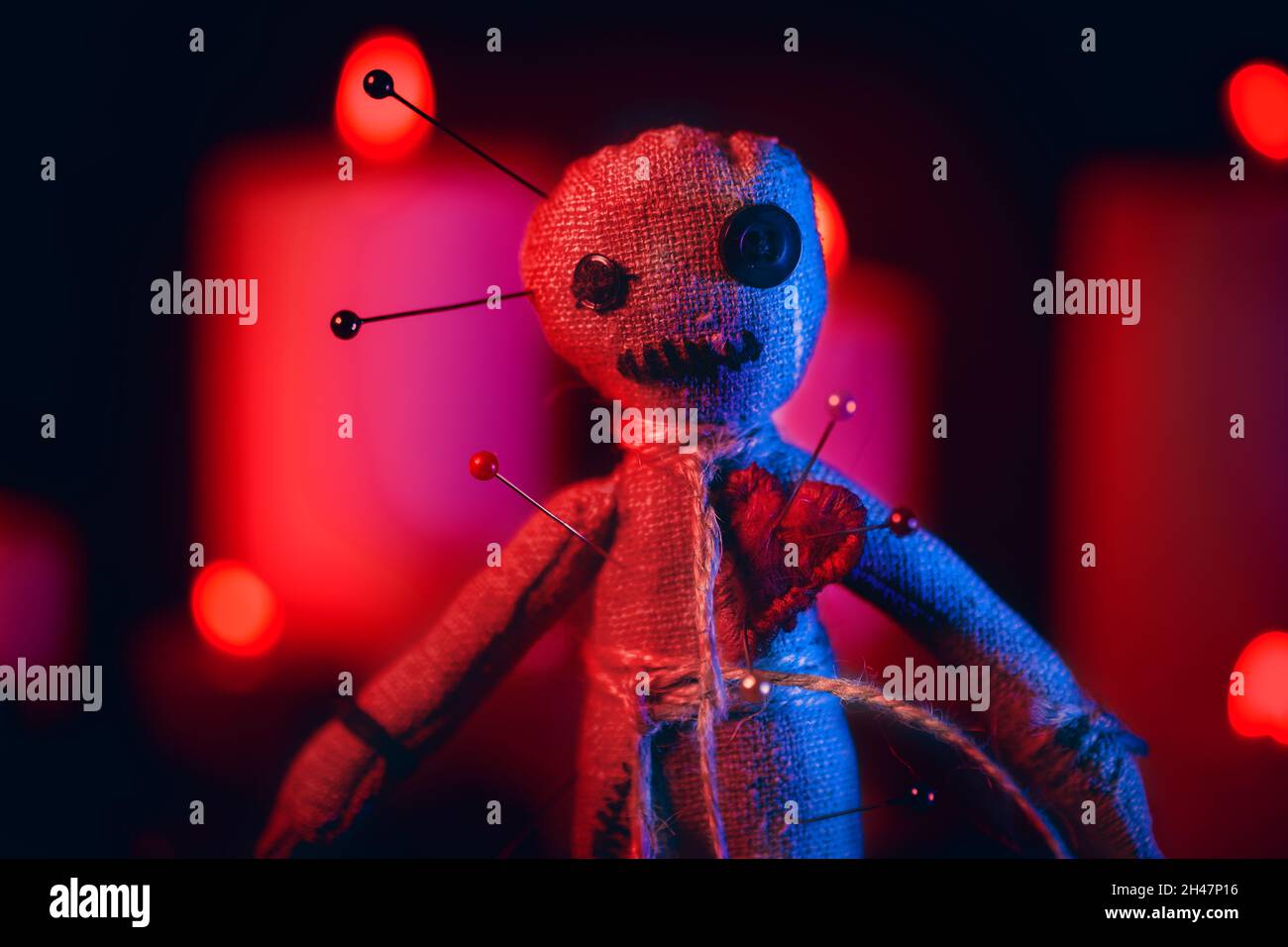 Voodoo Doll con aghi in rosso drammatico illuminazione da vicino. Foto Stock