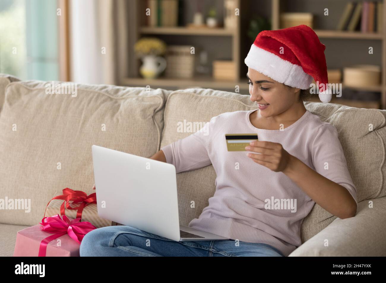 Felice bella giovane donna indiana che acquista regali di Natale online. Foto Stock