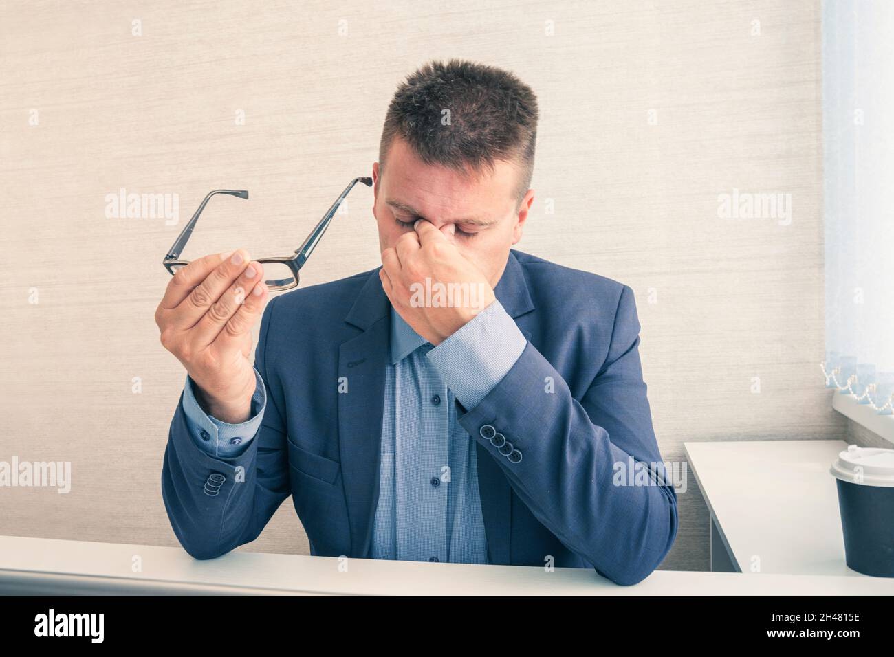 Lavorare da casa, affaticati o sotto sforzo. Il giovane asiatico si siede sulla scrivania. Sentirsi stanco stressato, tenere il naso. Chiudere gli occhi dopo Foto Stock