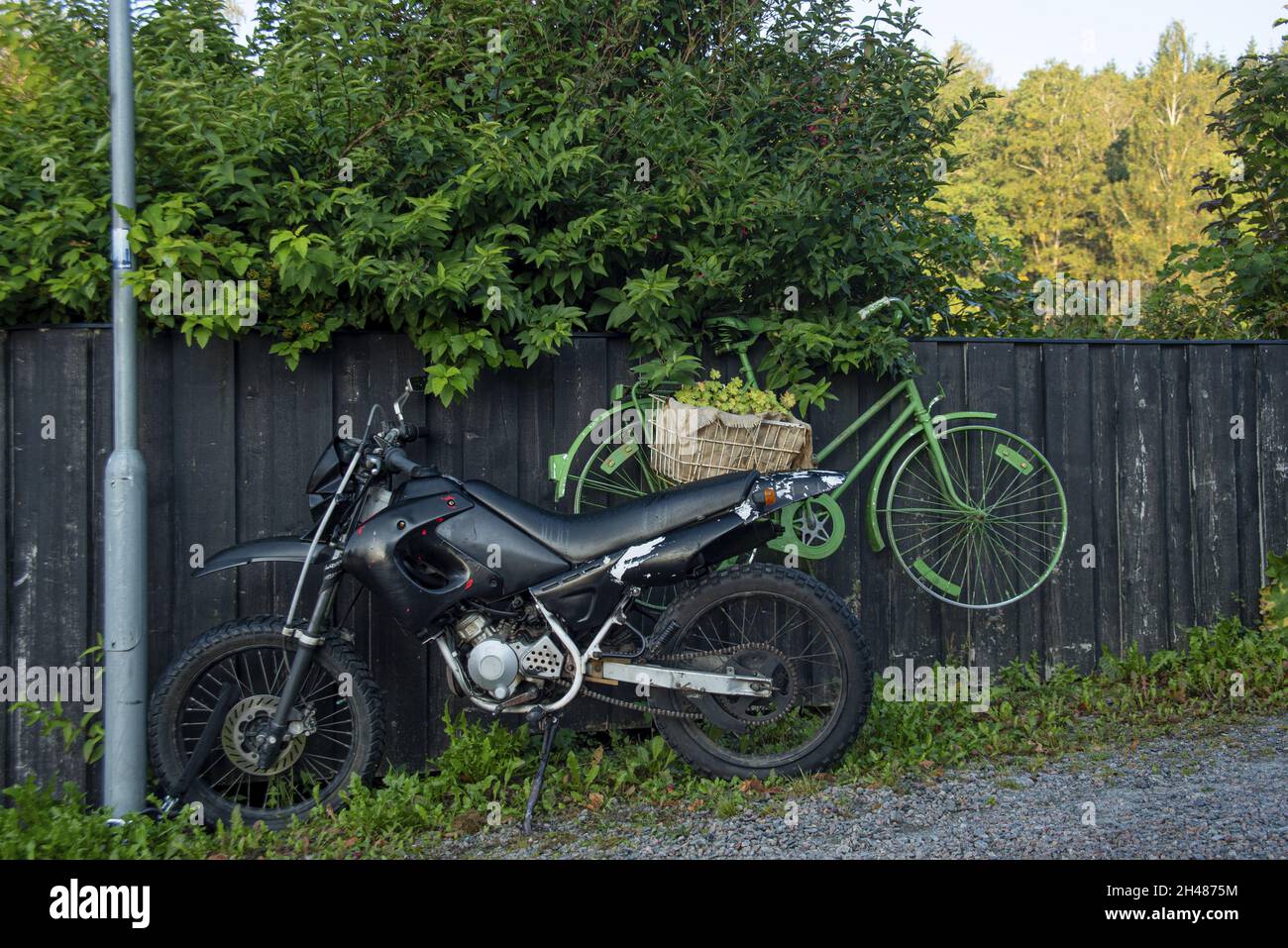 Motocicletta nera e una bicicletta verde appesa accanto ad una recinzione nera Foto Stock