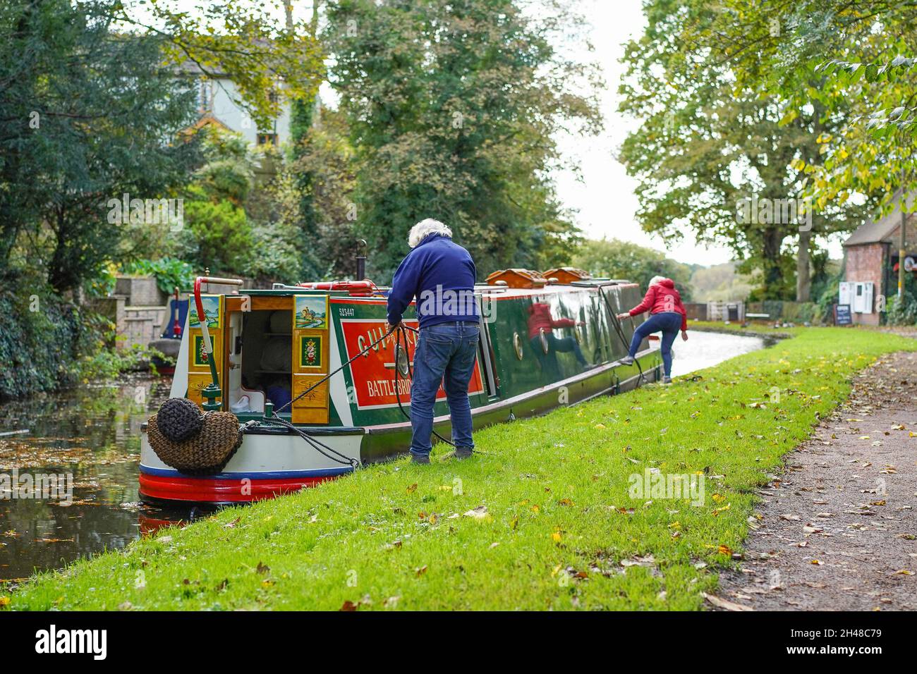 Uomo e donna ormeggiano una barca su un canale nelle Midlands durante l'autunno, Regno Unito. Foto Stock