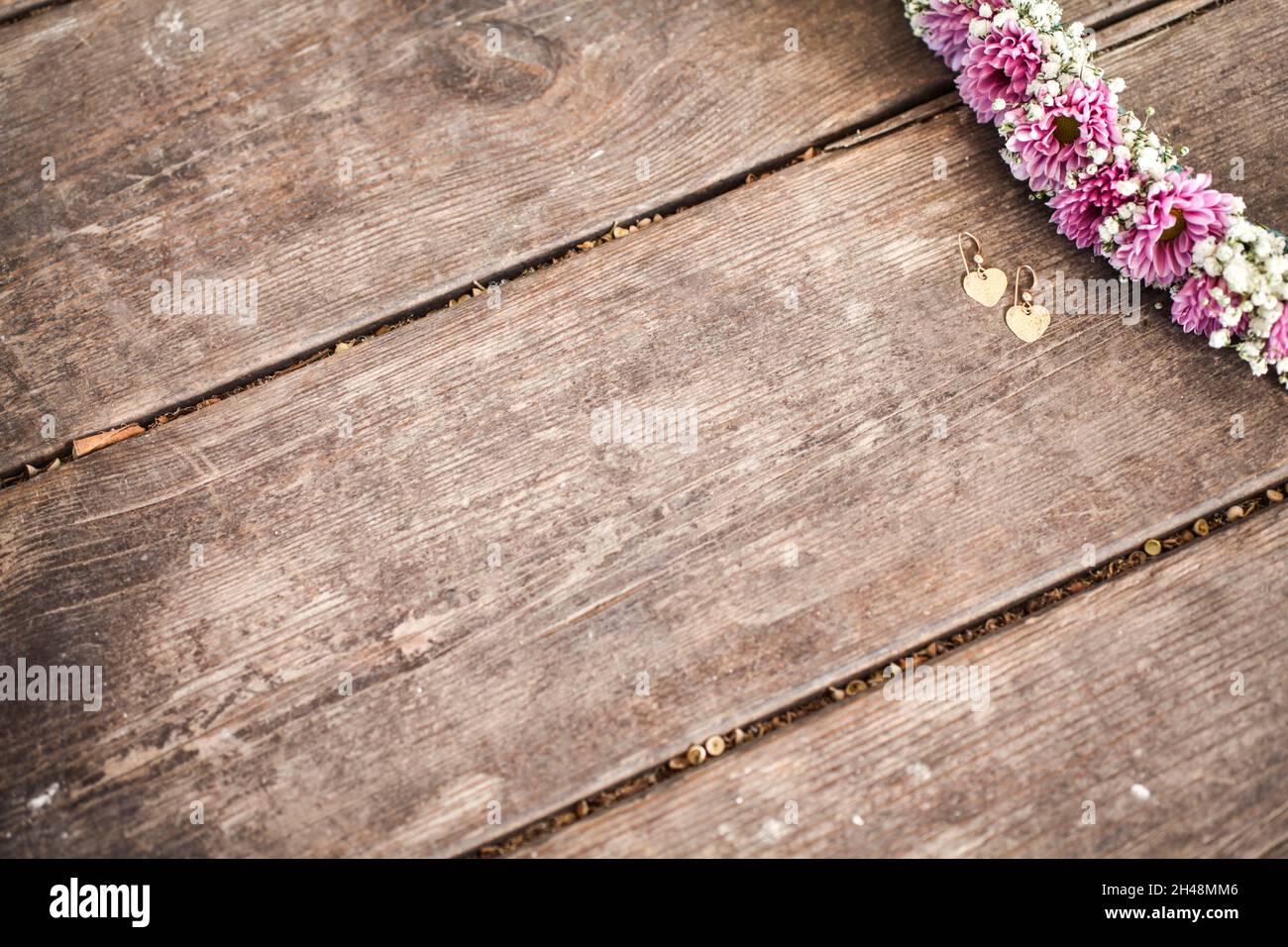 Cornice di fiori viola e malva su sfondo di legno con orecchini dorati Foto Stock