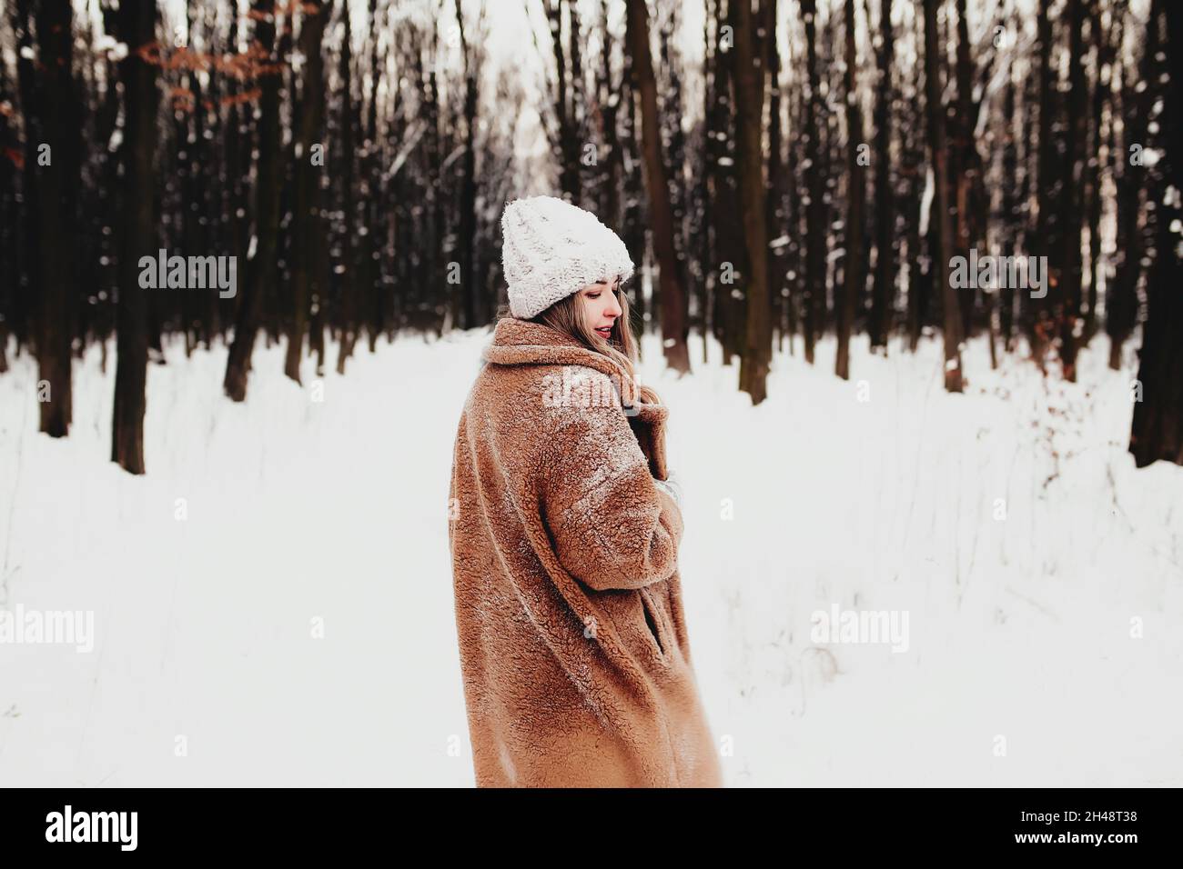 Foto di giovane bella donna in pelliccia di cappotto in piedi sulla neve bianca nella foresta invernale. La ragazza sorride e felice con gli occhi chiusi. La donna ha l'inverno Foto Stock