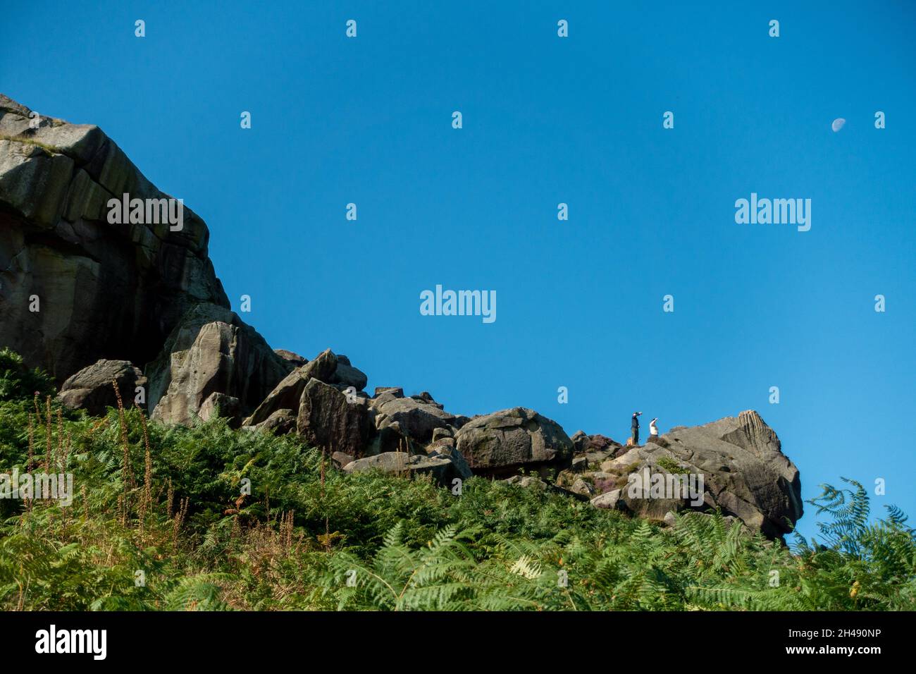 Persone che puntano da un punto di vista sulle rocce di mucca e vitello con la luna nel cielo, West Yorkshire, Regno Unito Foto Stock