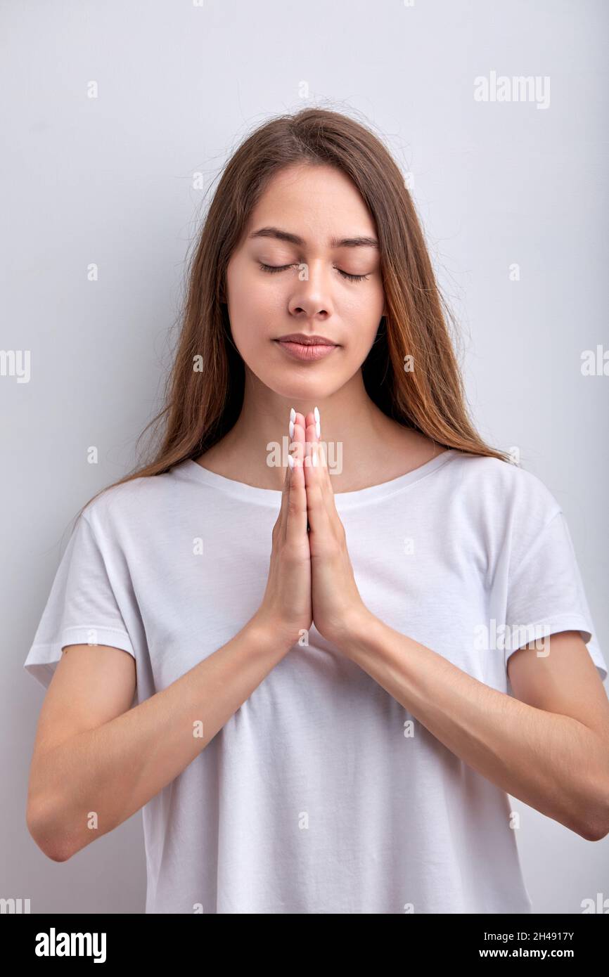 Calma donna caucasica tenere le mani insieme pregare con gli occhi chiusi isolato su sfondo bianco studio, ritratto di attraente signora in abiti casual t Foto Stock