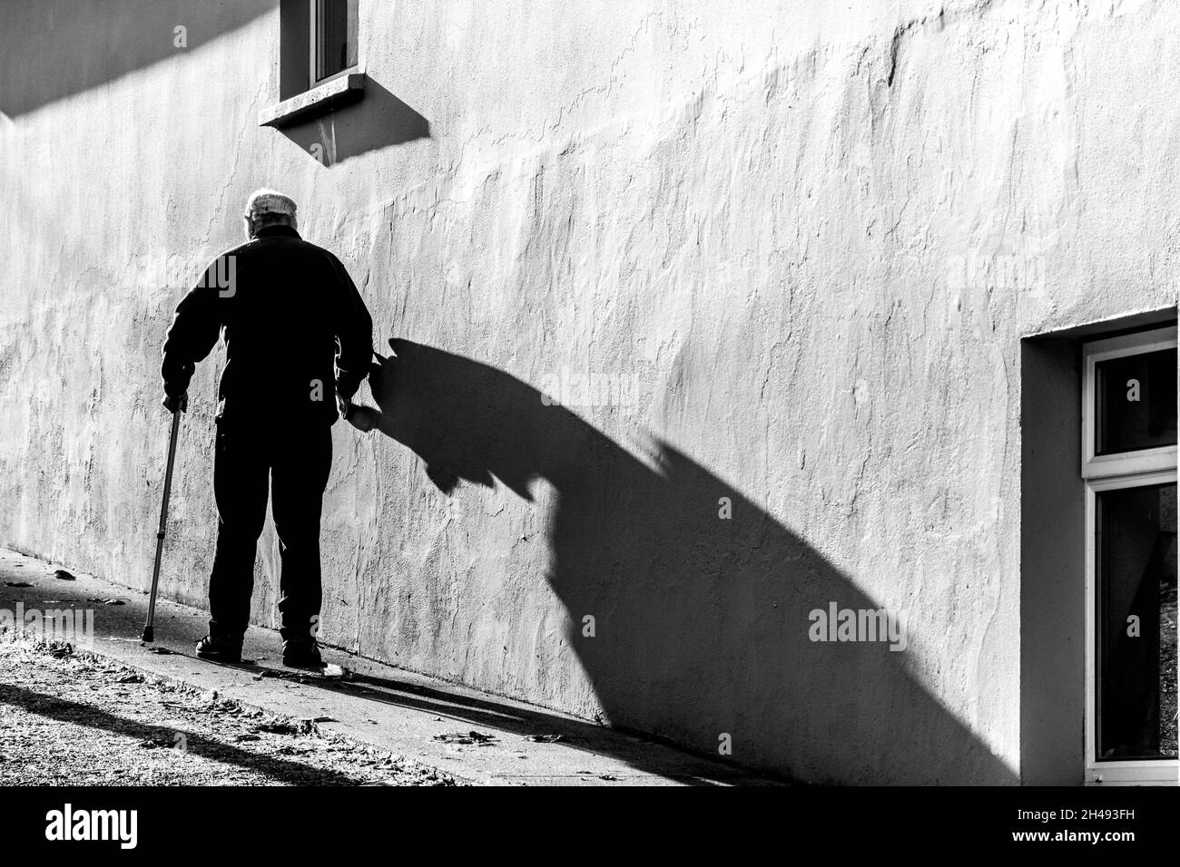 Anziano che cammina con il bastone e la sua ombra. Foto Stock