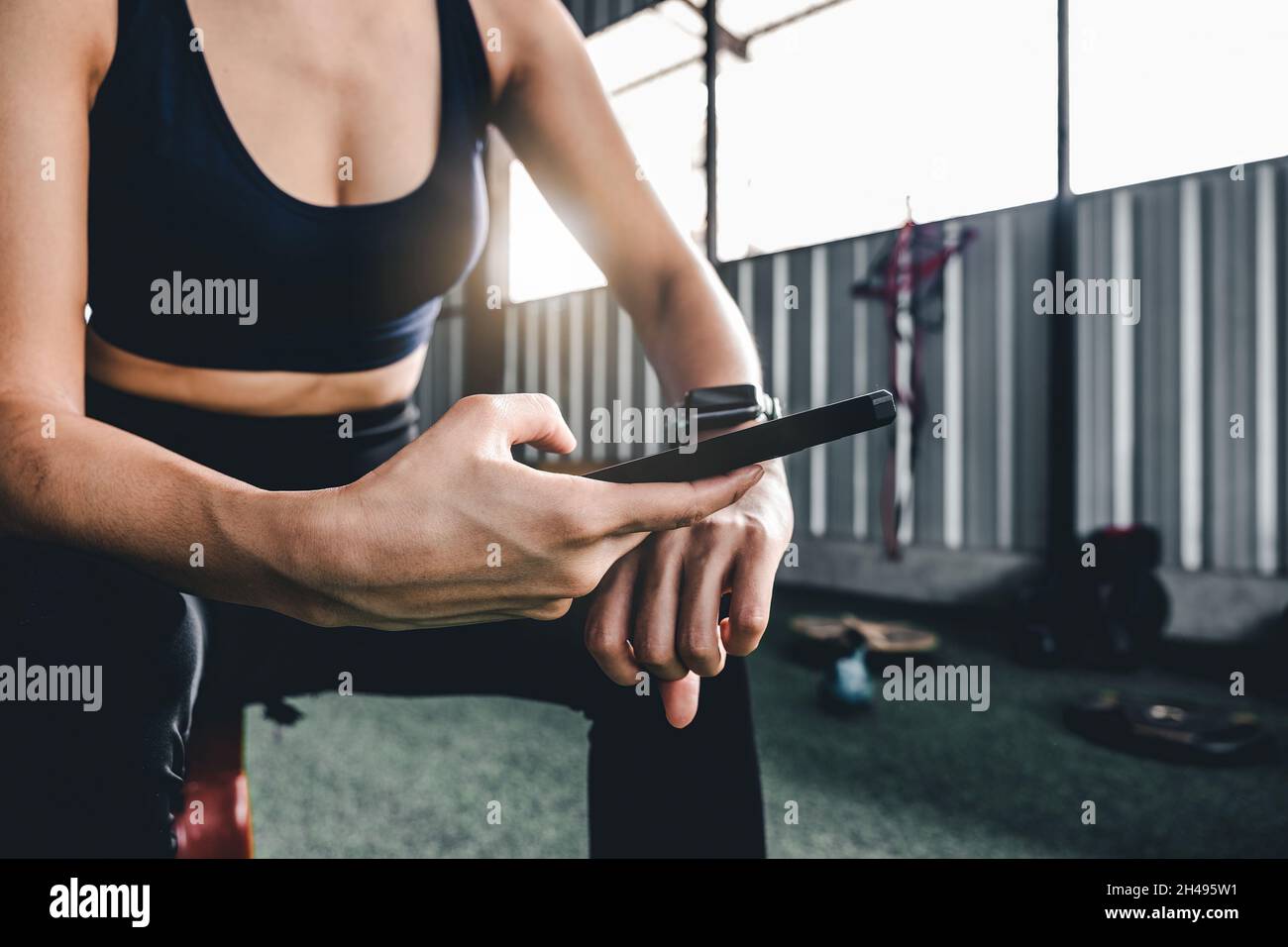Donna sportiva che riposa dopo l'allenamento durante l'uso dell'app per smartphone smartwatch Connect. Sfondo palestra interna. Concetto di sport di salute. Foto Stock