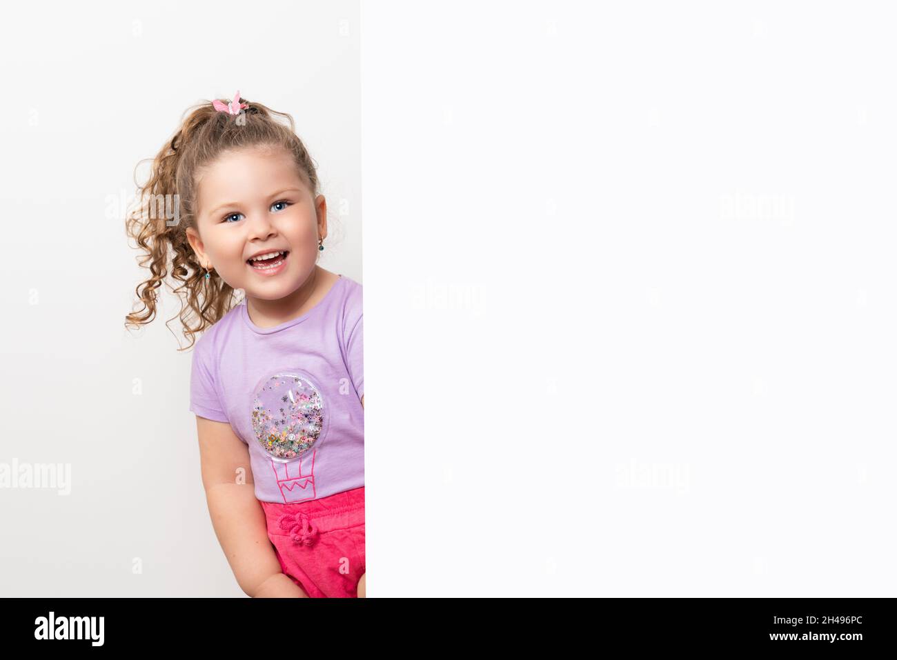 Sorridente occhio blu e carina bambina che sbuccia dietro una parete bianca. Foto di alta qualità Foto Stock