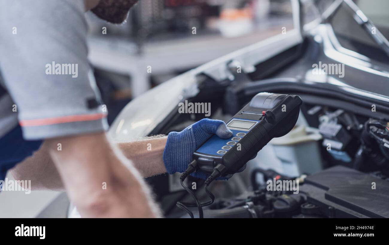 Meccanico professionista che fa un'ispezione dell'automobile, sta usando un tester della batteria Foto Stock