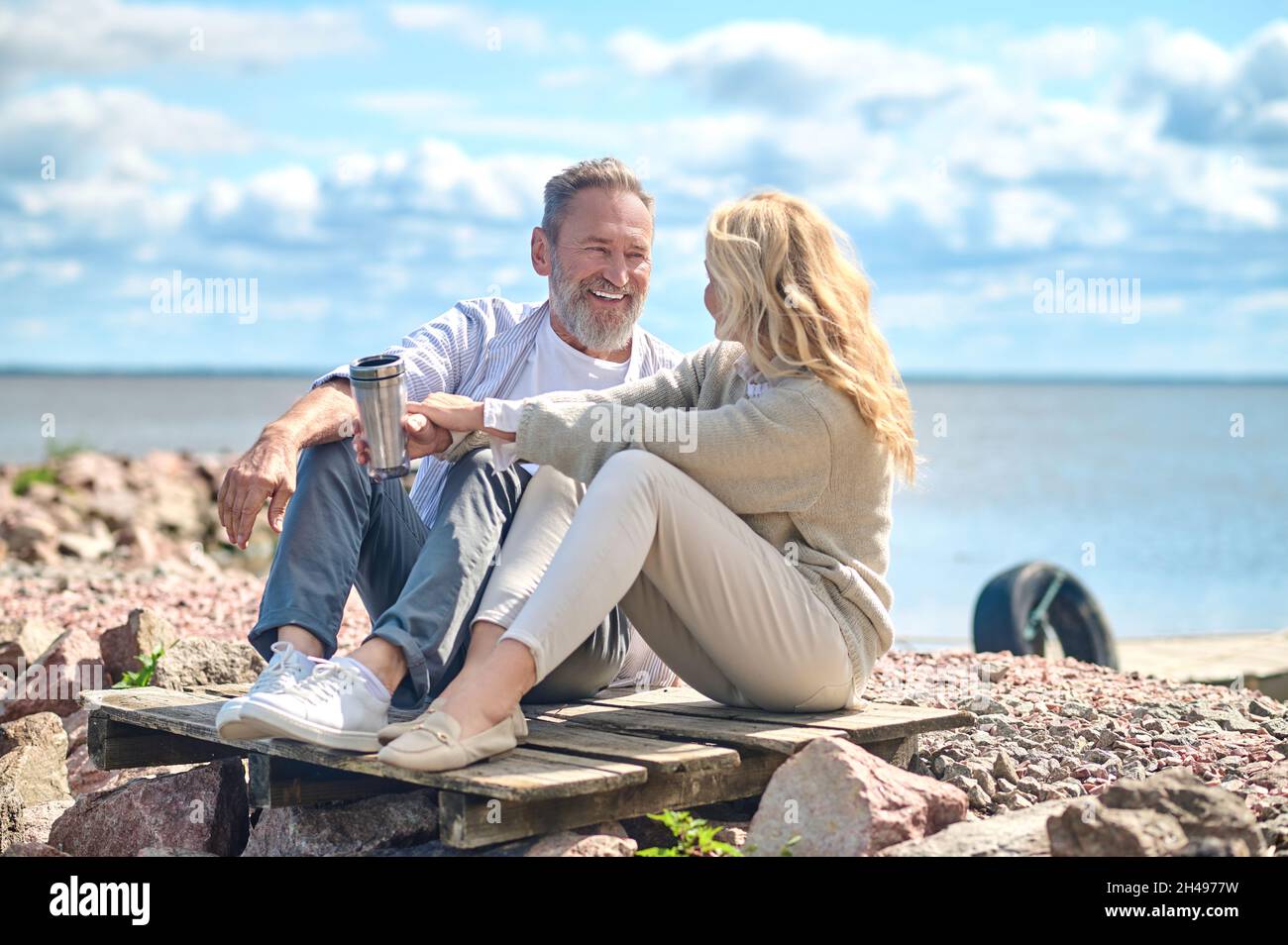 Comunicare uomo e donna seduti a terra vicino al mare Foto Stock