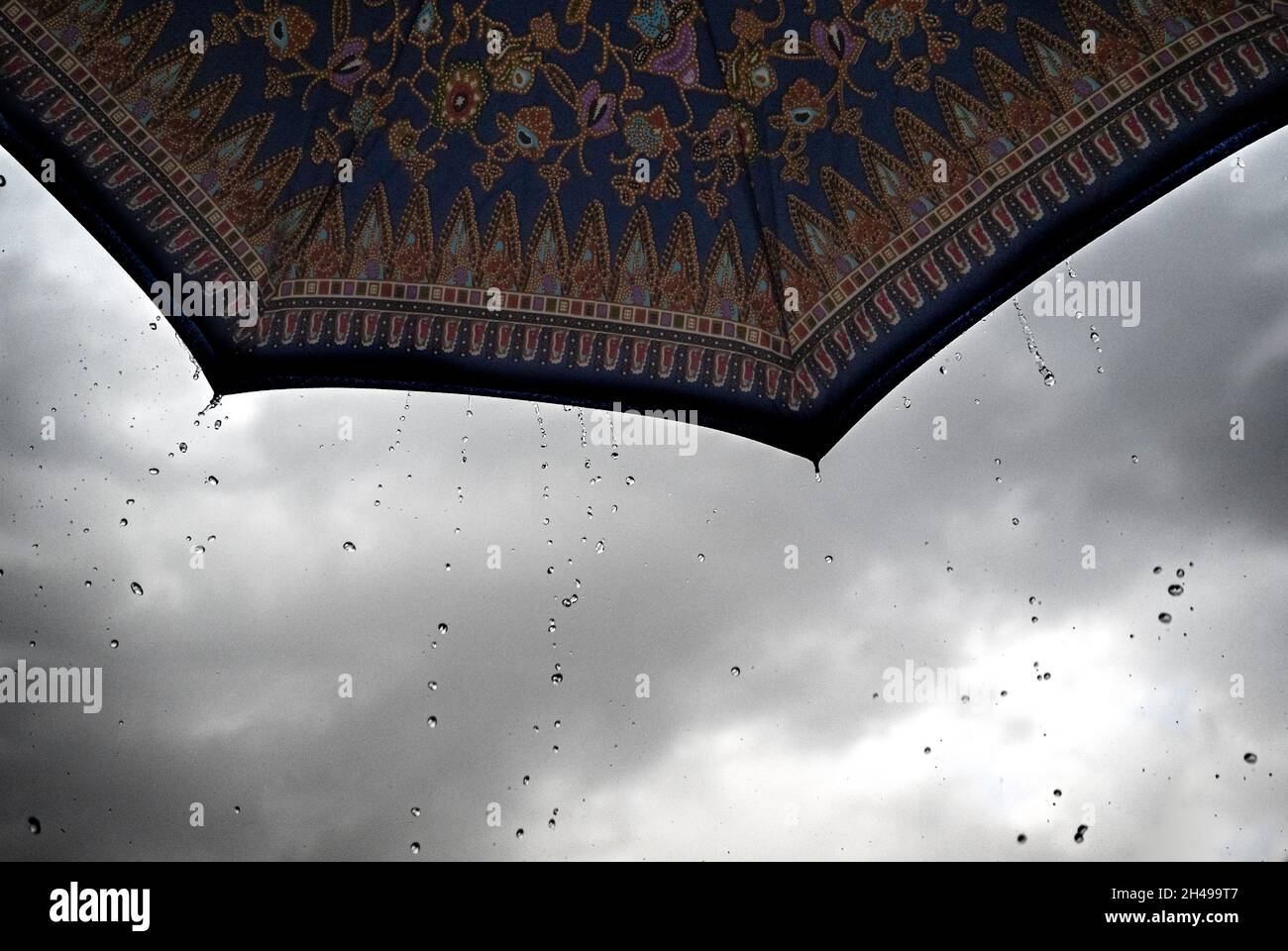 Gocce di pioggia che cadono da un ombrello stampato batik Foto Stock