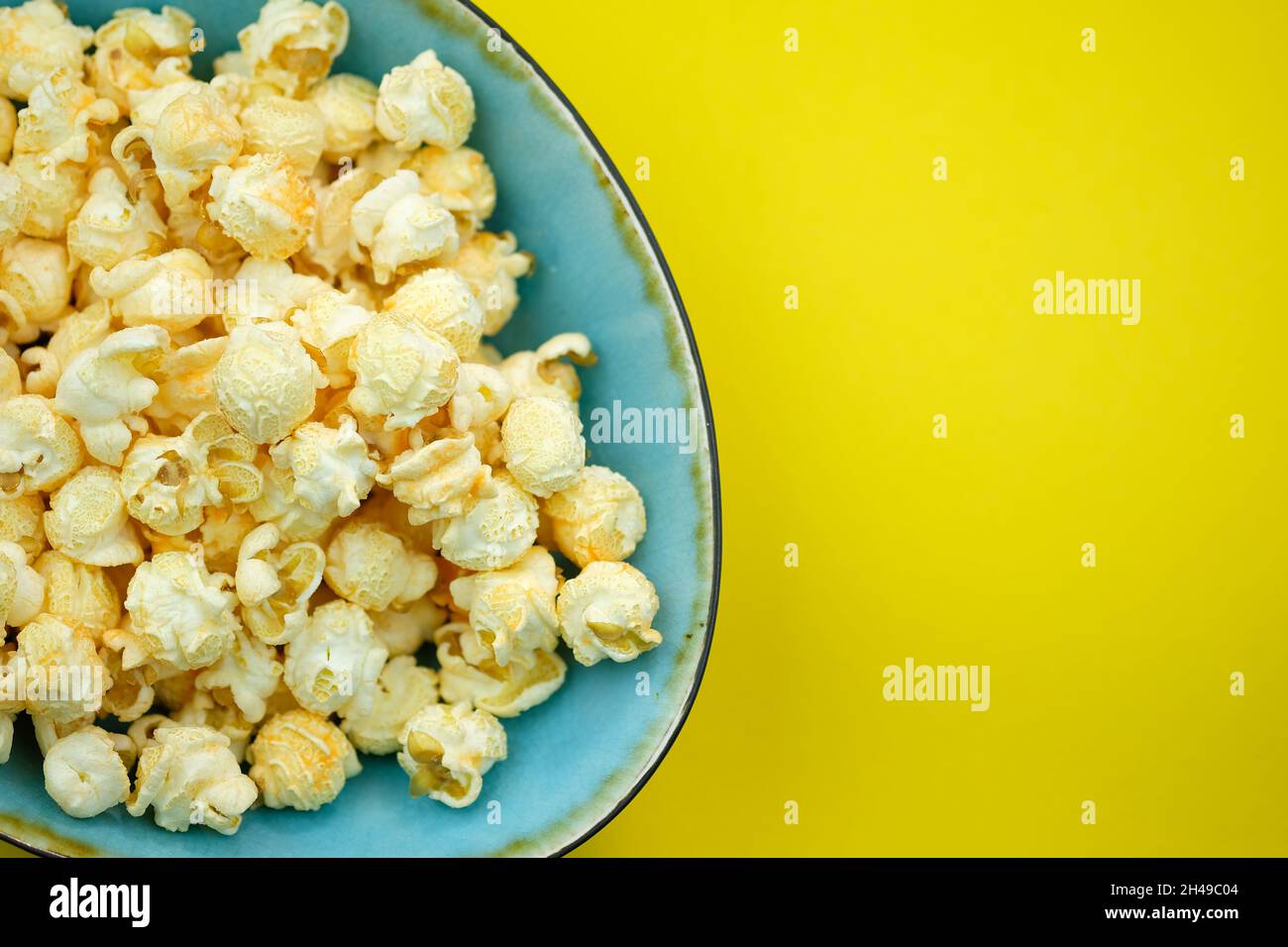 Popcorn con spezie in un piatto blu su sfondo giallo vista dall'alto. Popcorn salato con sapore di formaggio in una ciotola, luogo per il testo. Granaglie di mais da Ar Foto Stock