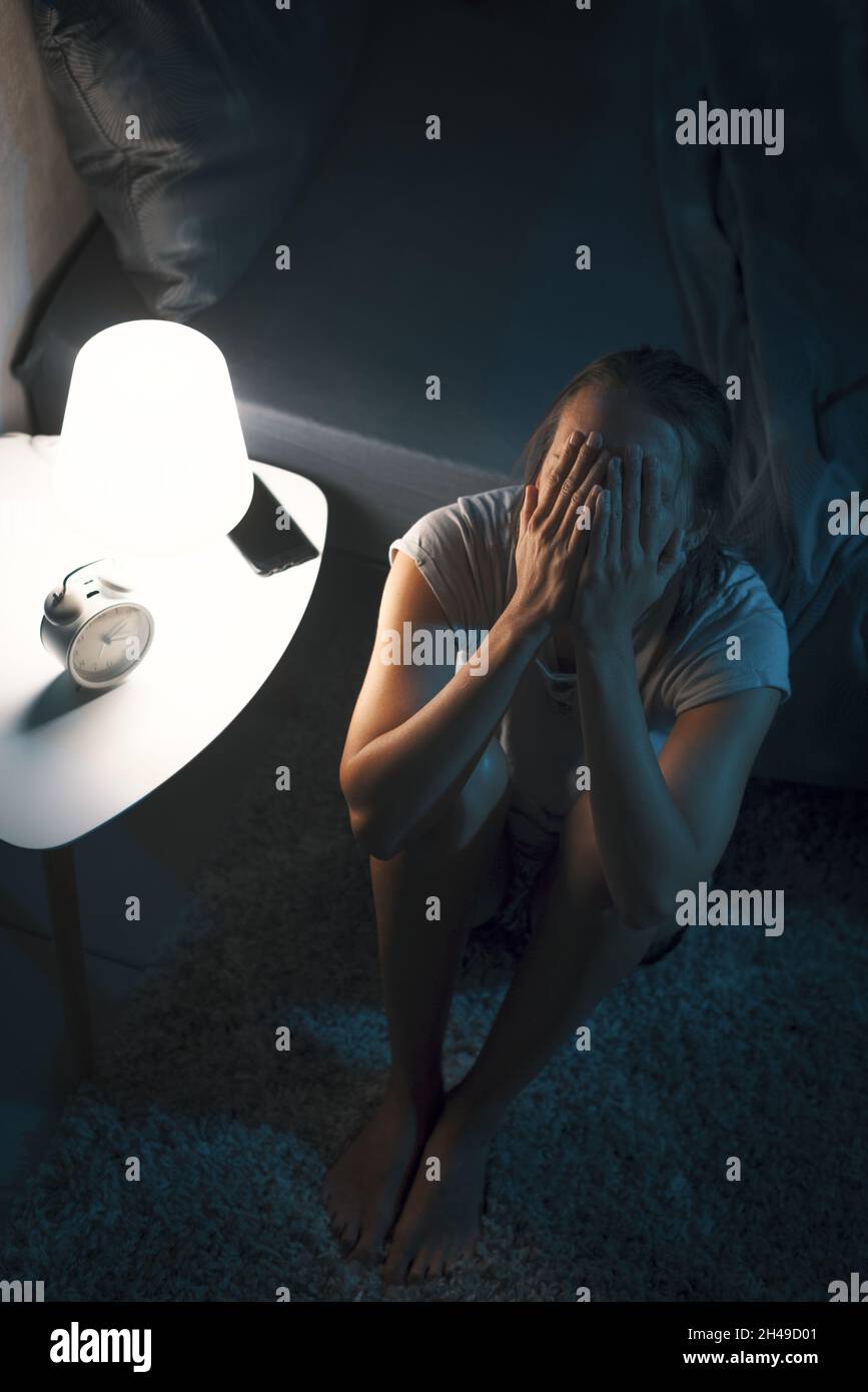 La giovane donna disperata si sveglia a tarda notte, non può dormire e ha un mal di testa, insonnia e stress concetto Foto Stock