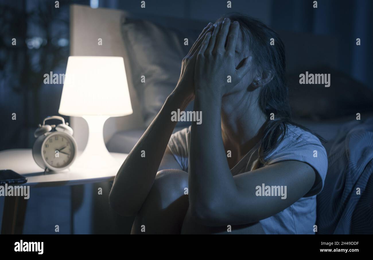 La giovane donna disperata si sveglia a tarda notte, non può dormire e ha un mal di testa, insonnia e stress concetto Foto Stock