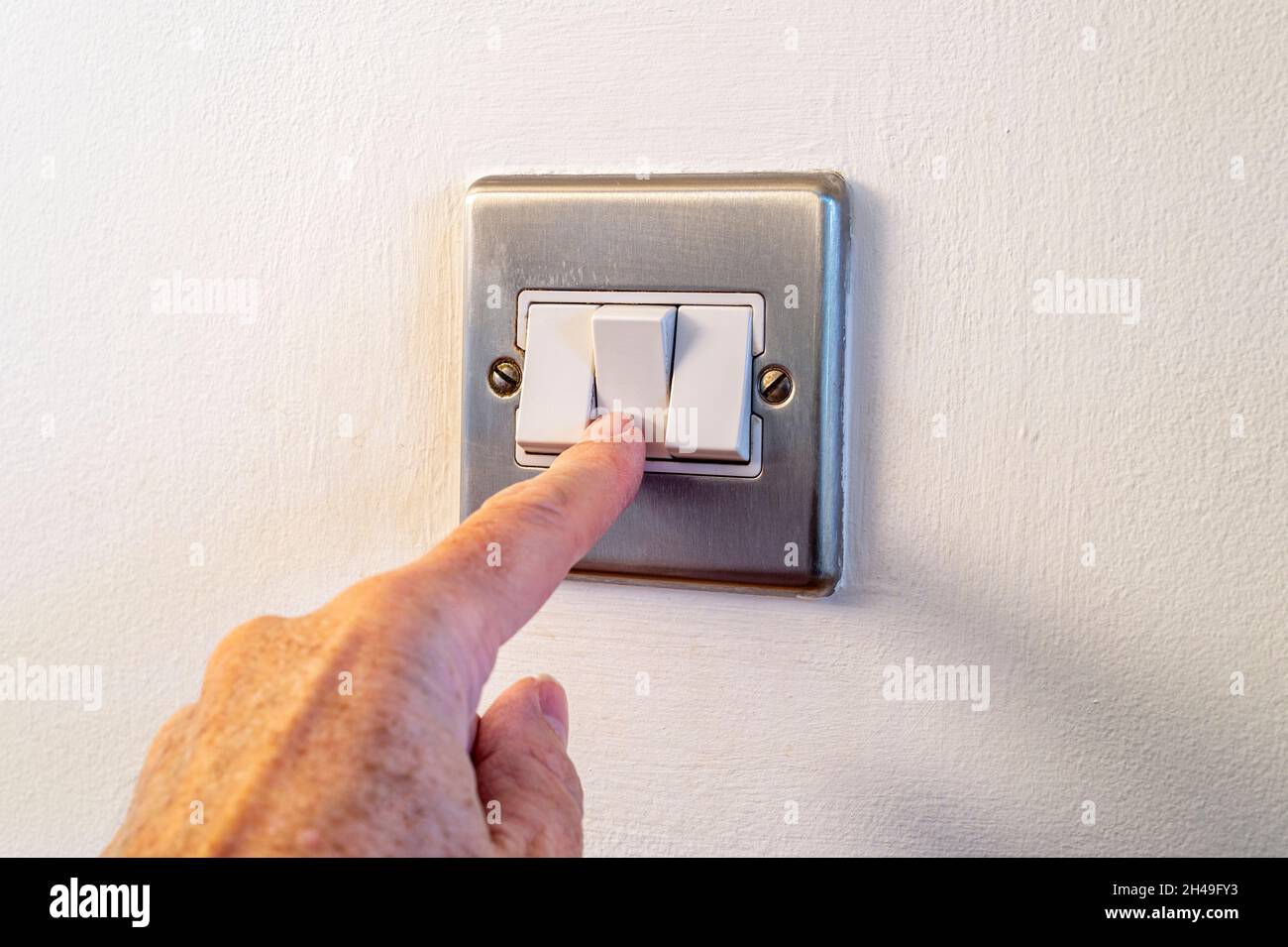 Primo piano di un dito maschio attivazione o disattivazione di un interruttore luci a casa. Alimentazione, energia, risparmio elettrico. Spazio di copia. Foto Stock