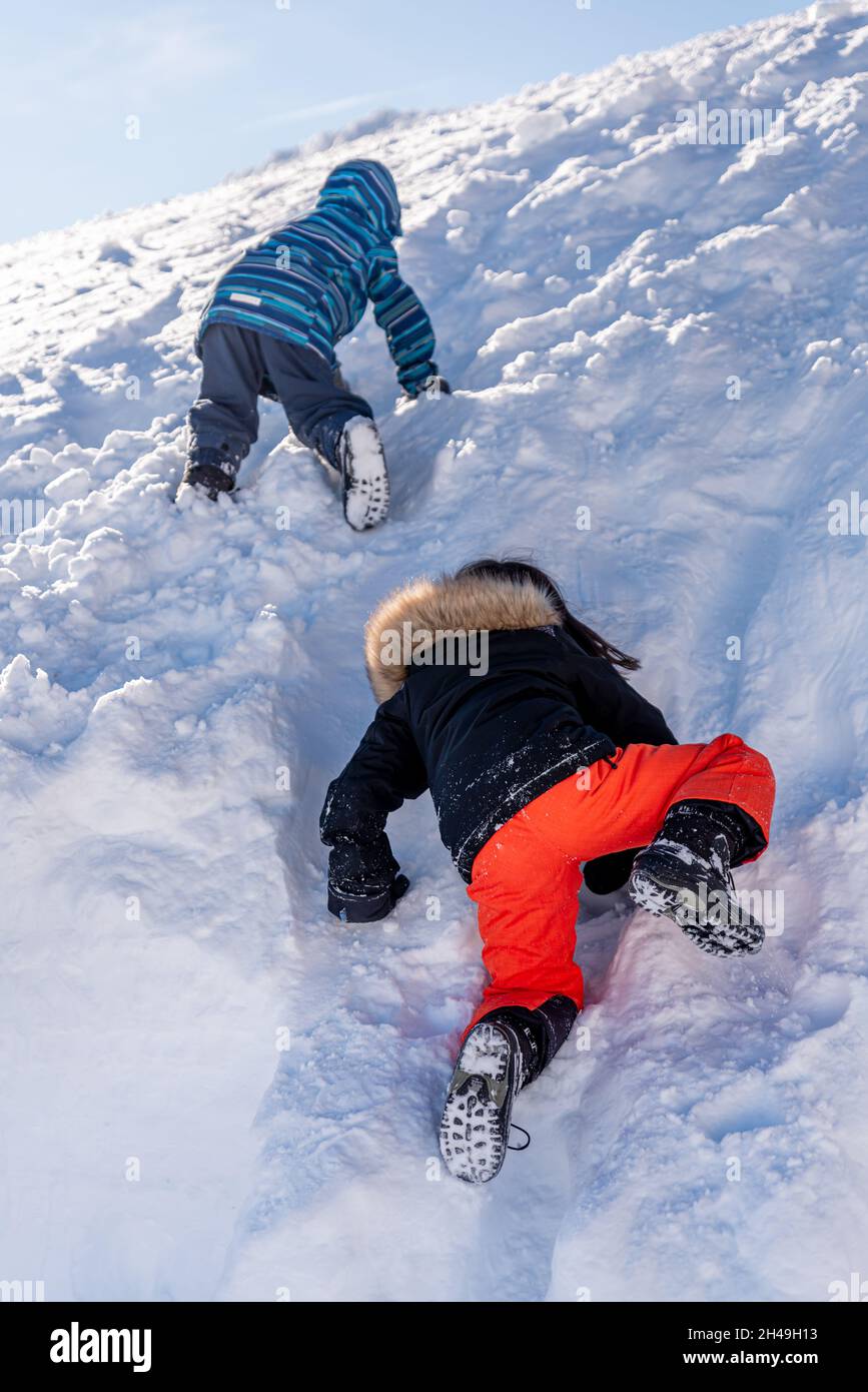 Bambini che giocano nella neve. Un ragazzo asiatico e una ragazza in sci-wear arrampicata in inverno. Buona infanzia. Foto Stock
