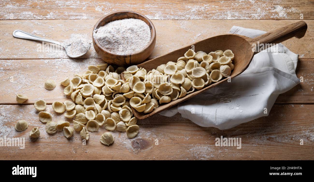 Orecchietta pugliese integrale. Orecchiette pugliesi in scoop con semola di grano duro intero su sfondo rustico in legno, primo piano. Foto Stock