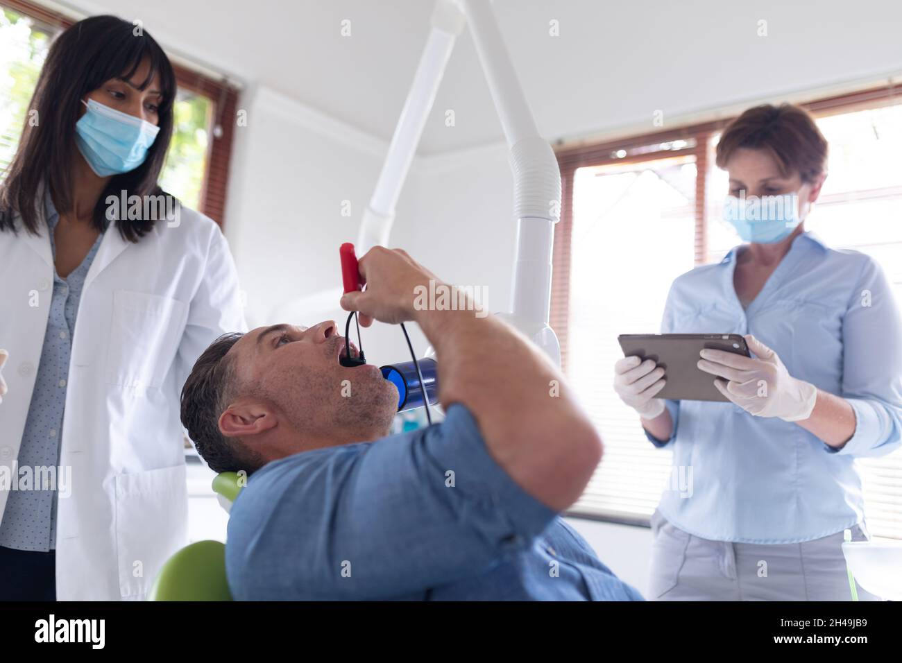 Dentista biraciale femminile con infermiere che esamina i denti di un paziente maschile nella moderna clinica dentale Foto Stock