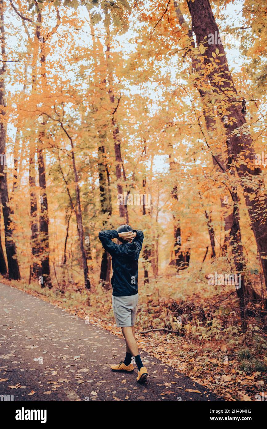 Giovane uomo misto-corsa si allunga dopo una corsa nei boschi nella caduta tra foglie gialle e arancioni. Riposo e recupero dopo un percorso sentiero sul sentiero del parco Foto Stock