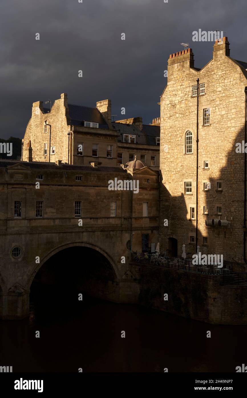 Edifici illuminati dal sole che circondano Pulteney Bridge sul fiume Avon nella storica città di Bath nel Regno Unito Foto Stock