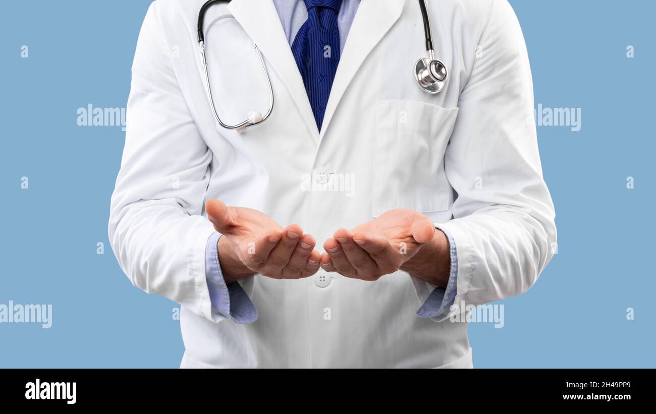 Irriconoscibile medico di sesso maschile che mostra oggetto invisibile alla medicina della pubblicità della fotocamera, tenendo qualcosa sulle mani sfondo blu studio. Panorama, Foto Stock