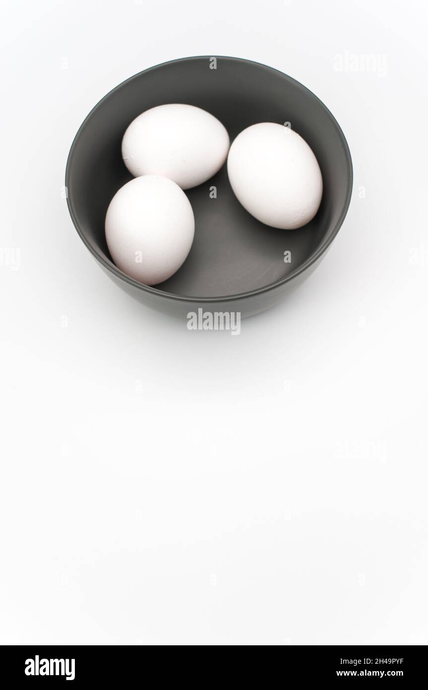 uova bianche isolate in una ciotola di ceramica scura su uno sfondo bianco con spazio di testo Foto Stock