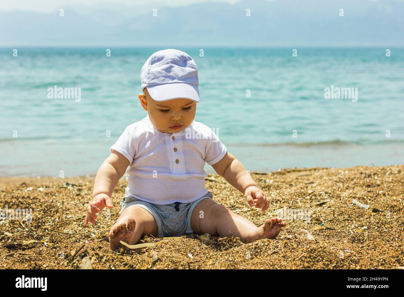 Carino ragazzino seduto sulla spiaggia di sabbia vicino al mare Foto Stock