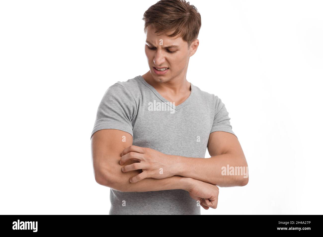 Infelice giovane maschio caucasico soffrono di irritazione e graffiare la pelle a portata di mano con espressione dolorosa, isolato su sfondo bianco. Reazione allergica Foto Stock