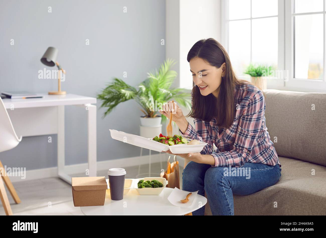 Donna soddisfatta che mangia pasto sano equilibrato o insalata in vassoio consegnato dal servizio di consegna cibo. Foto Stock