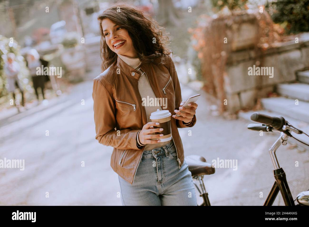 Bella giovane donna con cellulare bere caffè per andare in bicicletta il giorno d'autunno Foto Stock