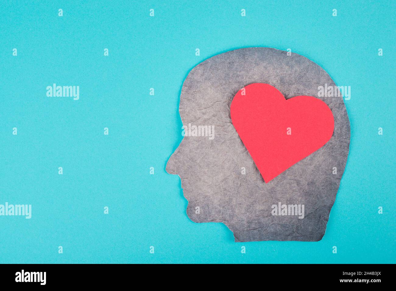 Silhouette di un volto con un cuore rosso, carta strapazzate, sfondo blu, spazio copia, amore simbolo emozione Foto Stock