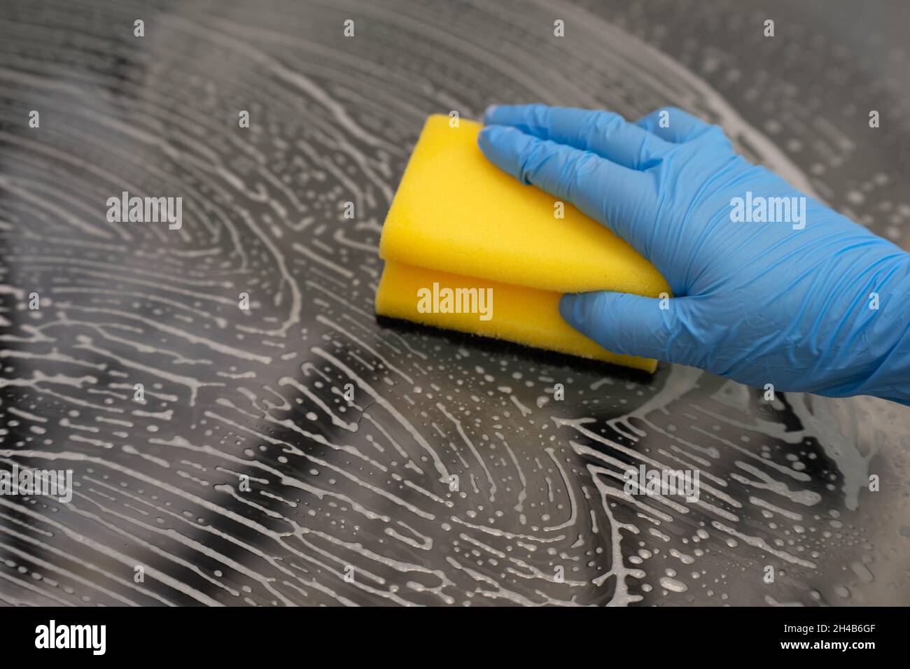 Utilizzare la superficie del vetro per il lavaggio dei guanti con spugna e schiuma detergente Foto Stock