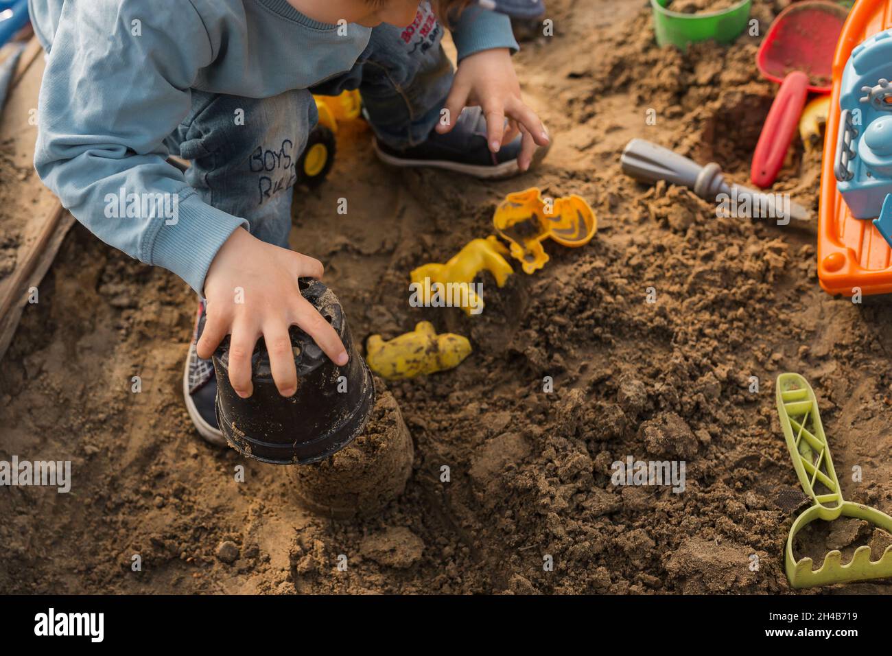 Mani di ragazzo che giocano in sandpit e fanno torta di fango Foto Stock