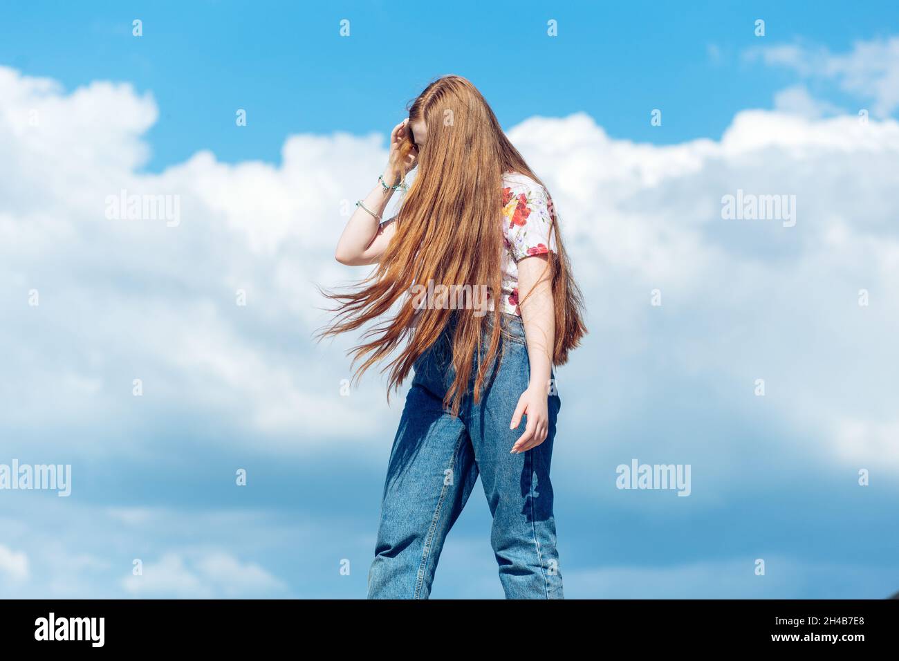 Ragazza di zenzero teen con i capelli lunghi in piedi sullo sfondo blu nuvoloso del cielo Foto Stock