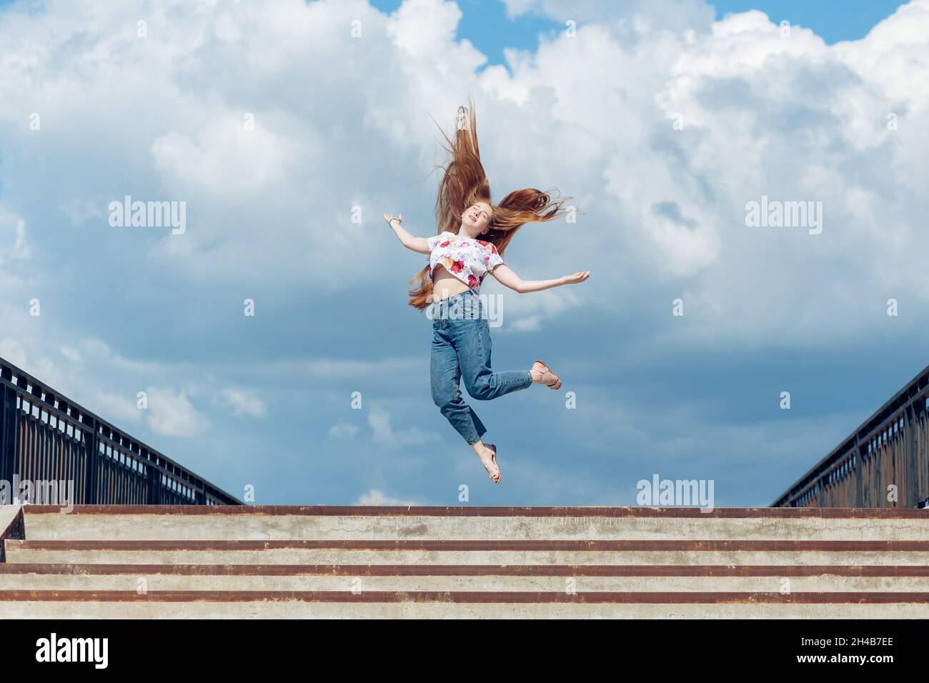 Giovane ragazza teen che salta su sullo sfondo blu del cielo nuvoloso Foto Stock