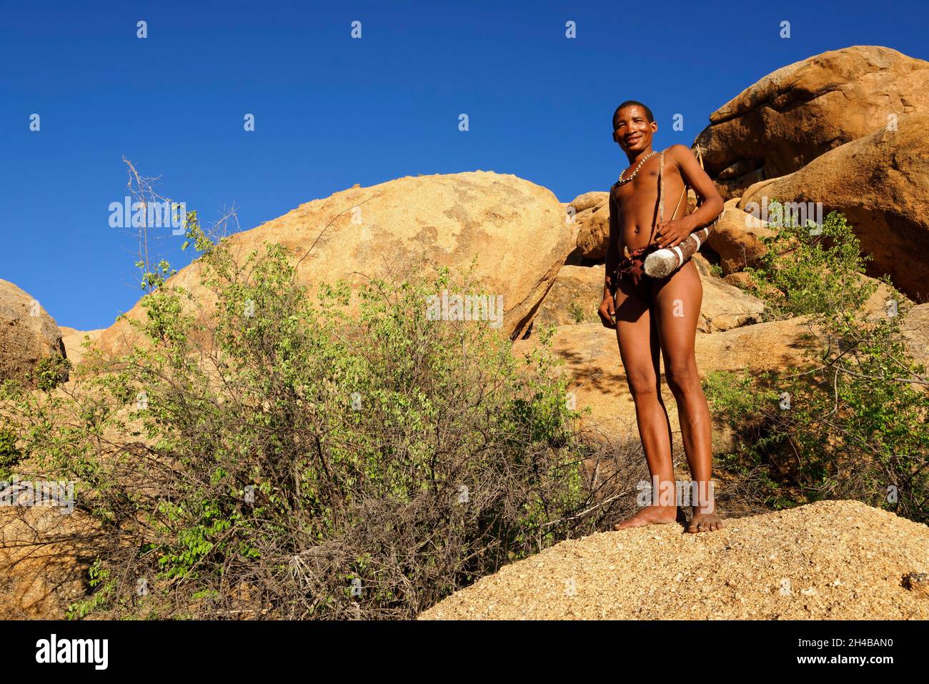 San Living Museum on Farm Omandumba (guest farm): San (Bushman) cacciatore in costume tradizionale con arco e freccia, sul rock Omaruru District Namibia Foto Stock