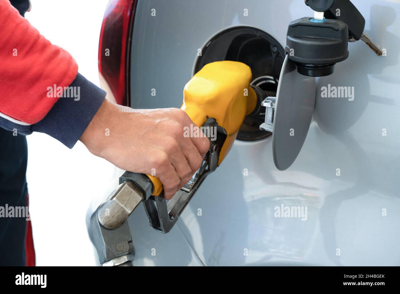 Pistola di rifornimento in mano dell'uomo, mentre si rifornisce l'auto con carburante a benzina, al concetto di stazione di servizio e carburante. Primo piano. Foto Stock
