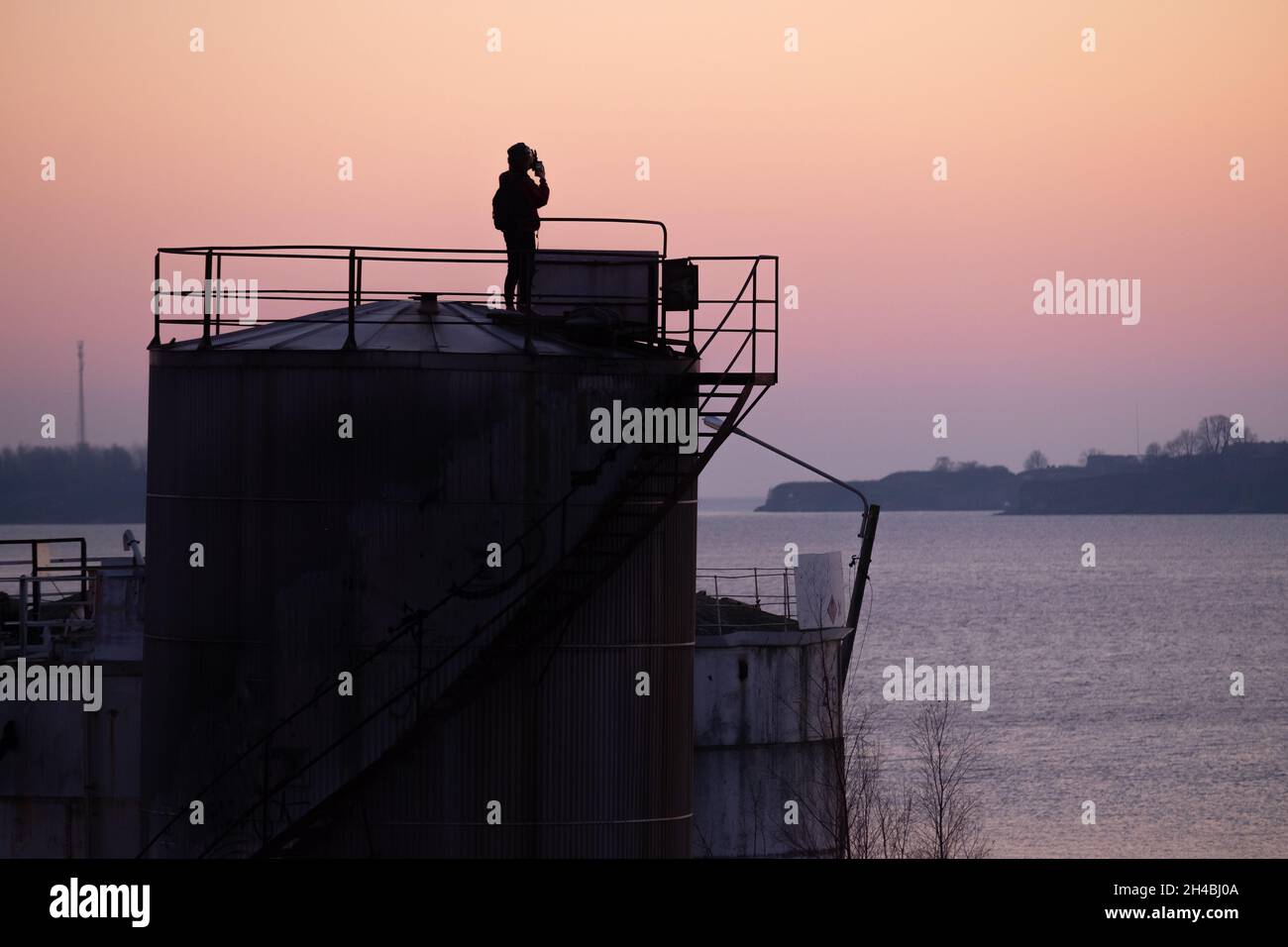 Helsinki / Finlandia - 1° NOVEMBRE 2021: Una silhouette di un uomo da solo in cima a un serbatoio di stoccaggio del petrolio abbandonato durante il tramonto. Foto Stock
