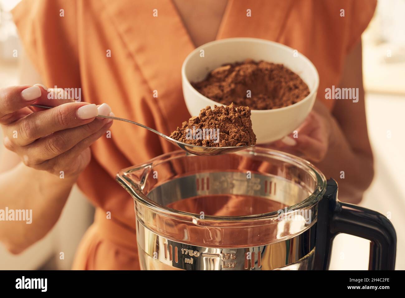 Mani di donna mettere cucchiaio di cacao in polvere nel frullatore elettrico prima di mescolarlo con altri ingredienti Foto Stock