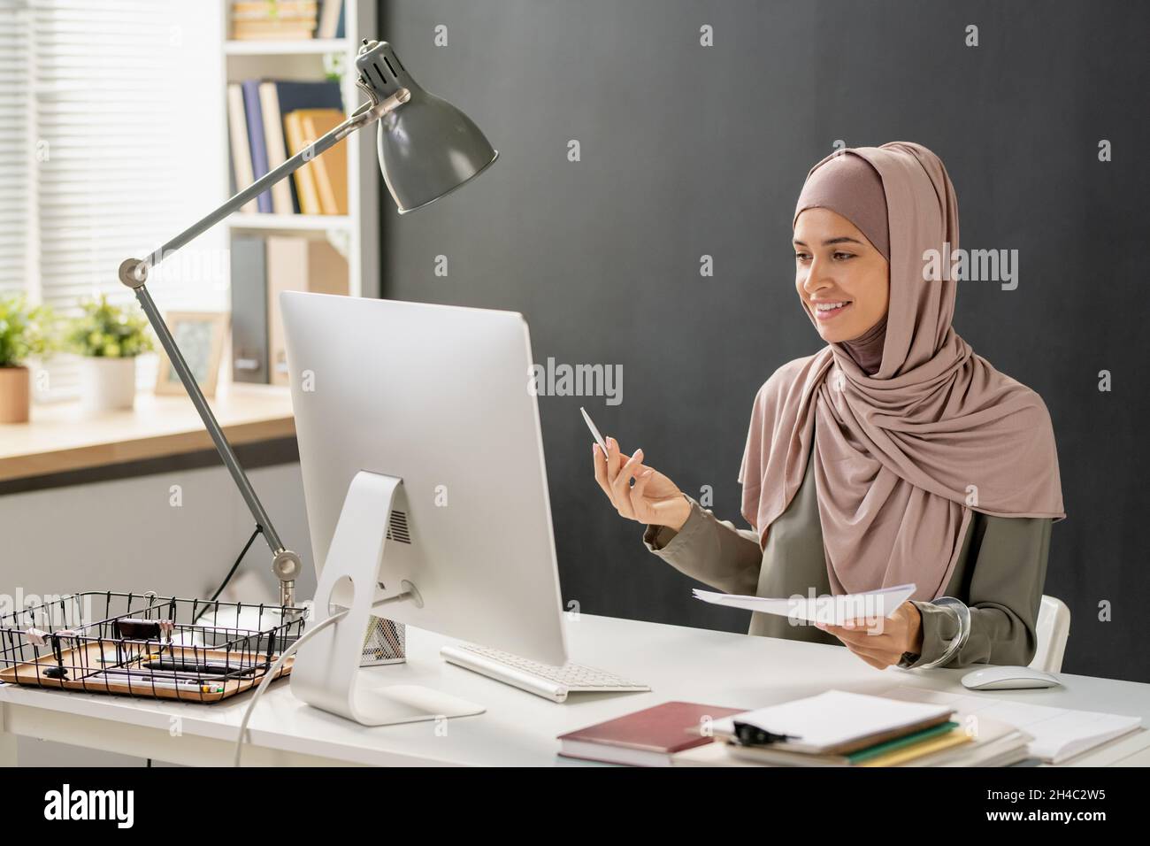 Felice giovane donna musulmana che parla con l'insegnante sullo schermo del computer durante la lezione online in ambiente d'ufficio Foto Stock