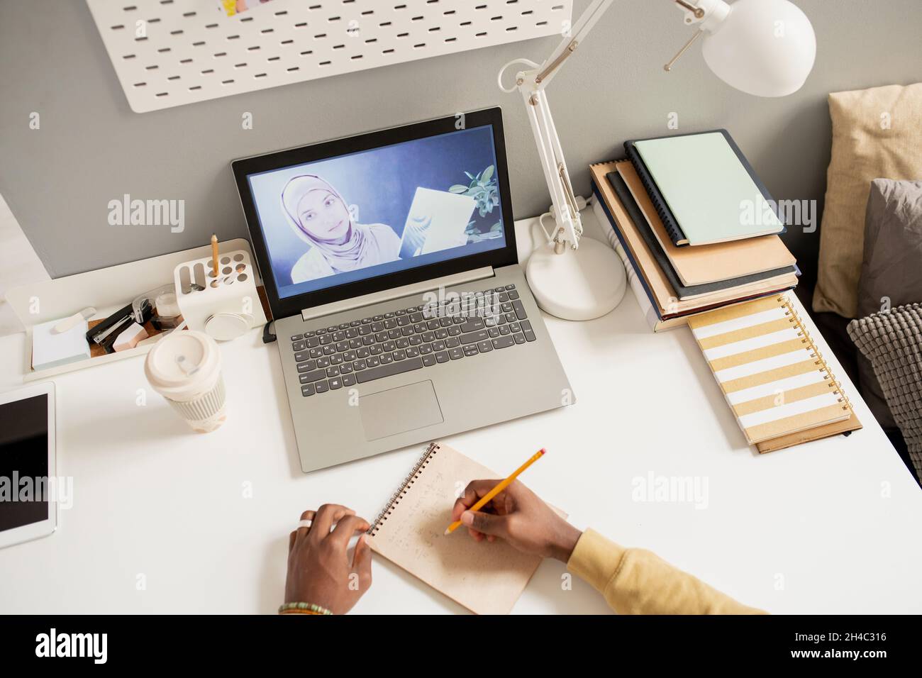 Giovane insegnante fiducioso in hijab sullo schermo del portatile e le mani dello studente africano che fanno appunti durante la lezione online Foto Stock