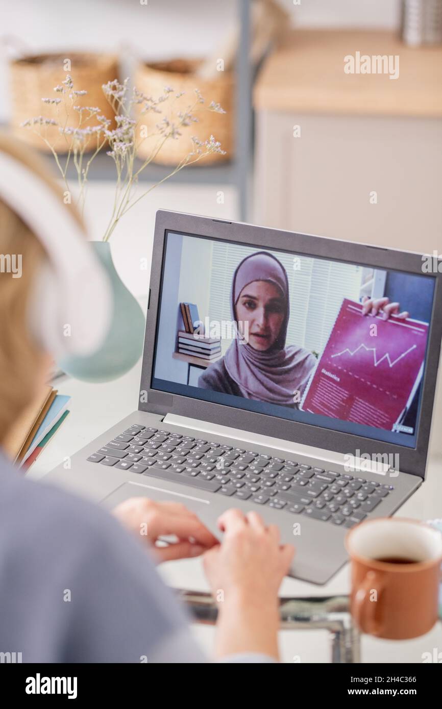 Giovane musulmana in broschermo di lapto che mostra il documento finanziario e spiega il grafico durante il corso di studio online Foto Stock