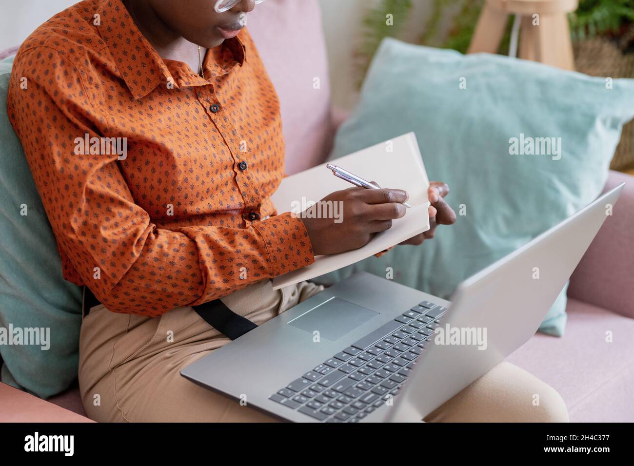 Mani di giovane studentessa africana con penna fare appunti di lezione in copybook durante il corso di studio online Foto Stock