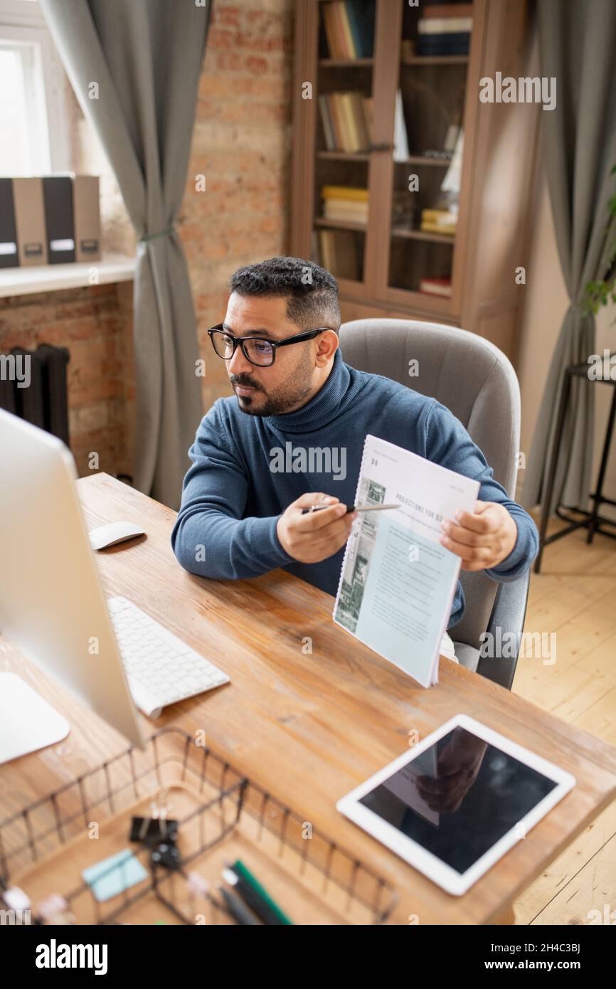 Insegnante sicuro che indica il documento mentre presenta e spiega i dati agli studenti durante la lezione online Foto Stock
