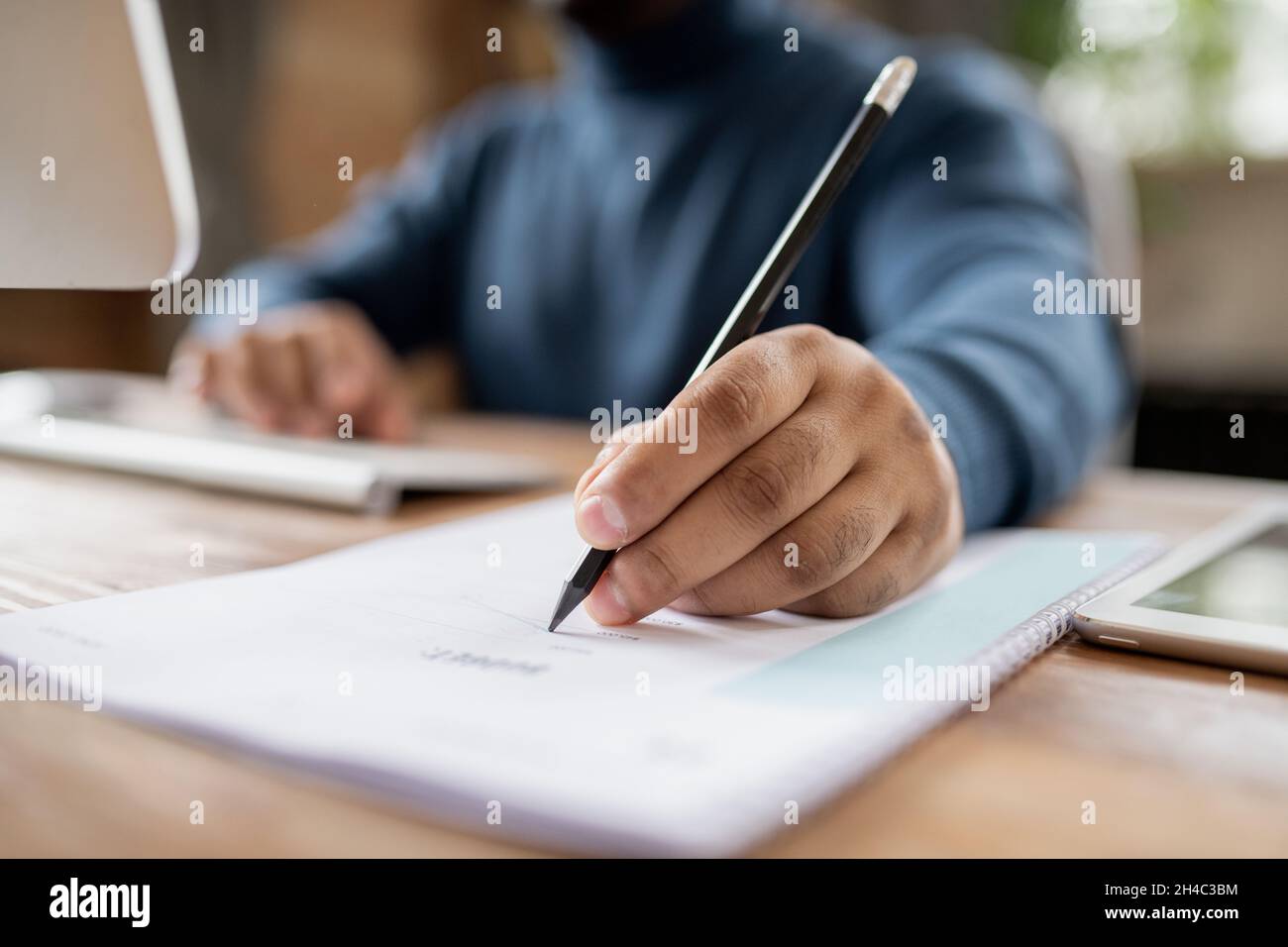 Mano dell'uomo che tiene la matita sopra il documento mentre si siede davanti al calcolatore e fa le note durante la lezione in linea Foto Stock