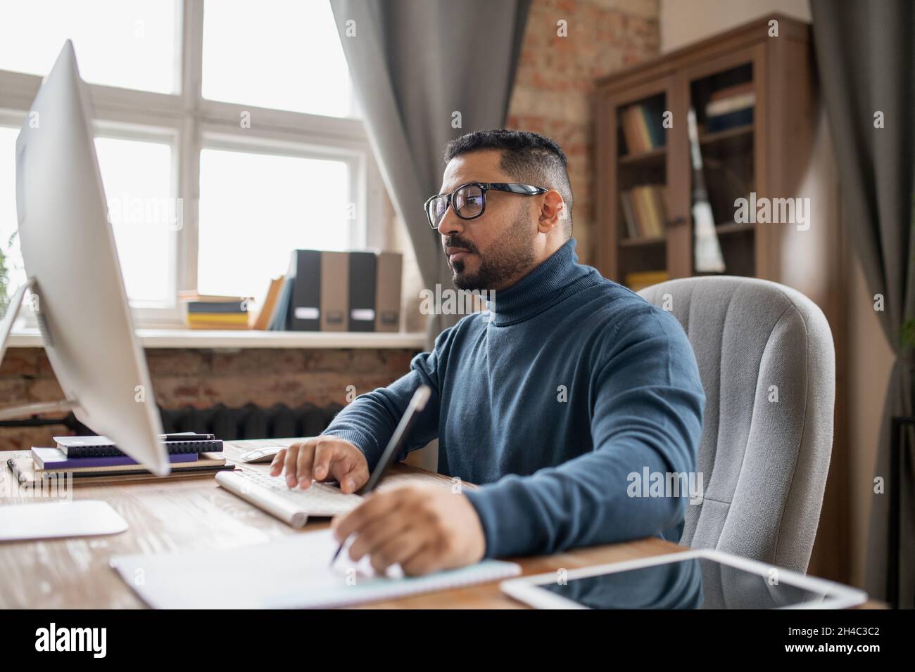 Uomo maturo serio premendo il tasto e guardando lo schermo del computer mentre si fa appunti durante la lezione online Foto Stock