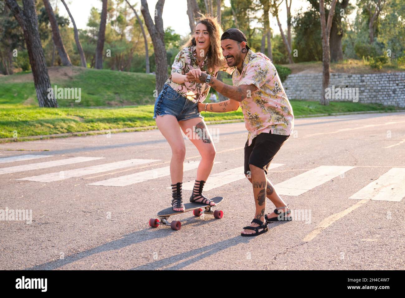 Giovane uomo fresco tatuato che insegna alla sua ragazza come skateboard. Foto Stock