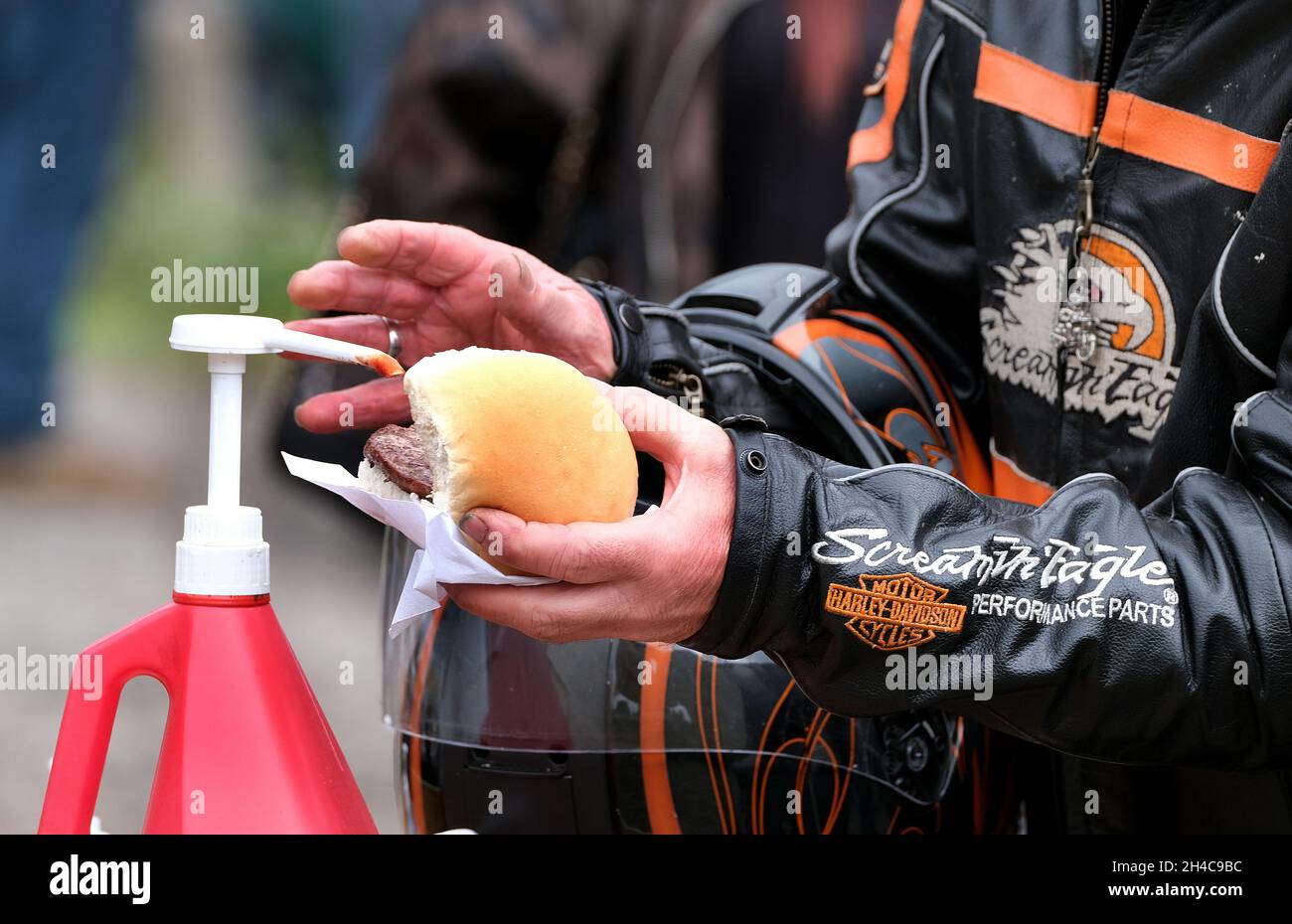 Biker aggiungere la salsa ad un hamburger in una panna a uno spettacolo di bici. Foto Stock