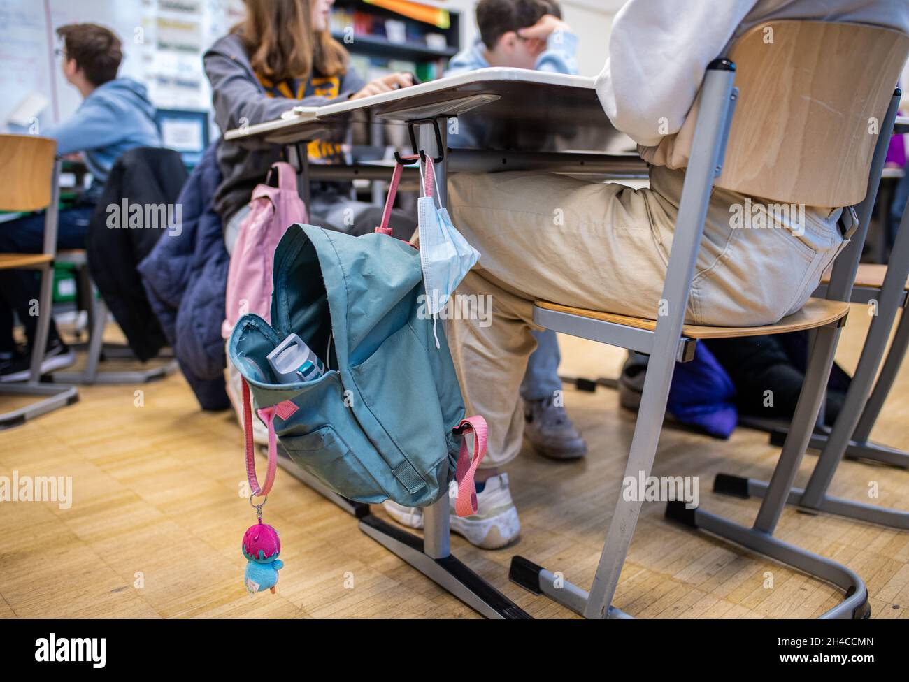 02 novembre 2021, Renania Settentrionale-Vestfalia, Münster: Nel 9° grado della scuola completa di Münster, una copertura bocca-naso appende su un tavolo di classe accanto ad uno zaino. Dal 02.11.2021 l'obbligo della maschera nelle scuole al posto in aula è caduto. Gli alunni della Renania Settentrionale-Vestfalia non devono indossare una maschera in classe da martedì, a condizione che si siedano a posti fissi. Tuttavia, il requisito della maschera si applica ancora sulla strada per il sedile e nell'edificio scolastico. Foto: Guido Kirchner/dpa Foto Stock