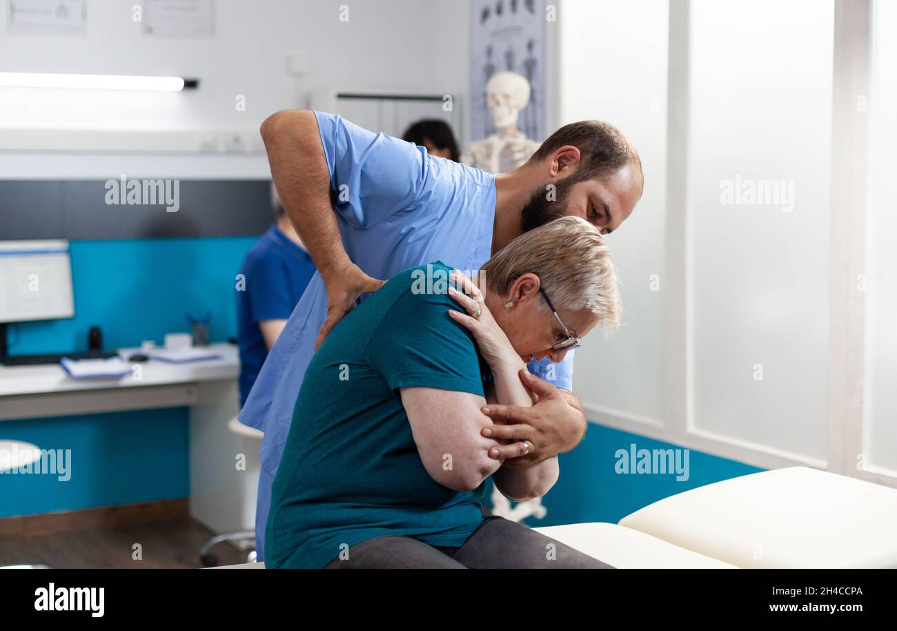 Assistente osteopatico che cracking schiena e spalle ossa per la donna anziana alla consultazione chiropratica. Chiropratico che fornisce assistenza al paziente anziano per il recupero e la riabilitazione Foto Stock